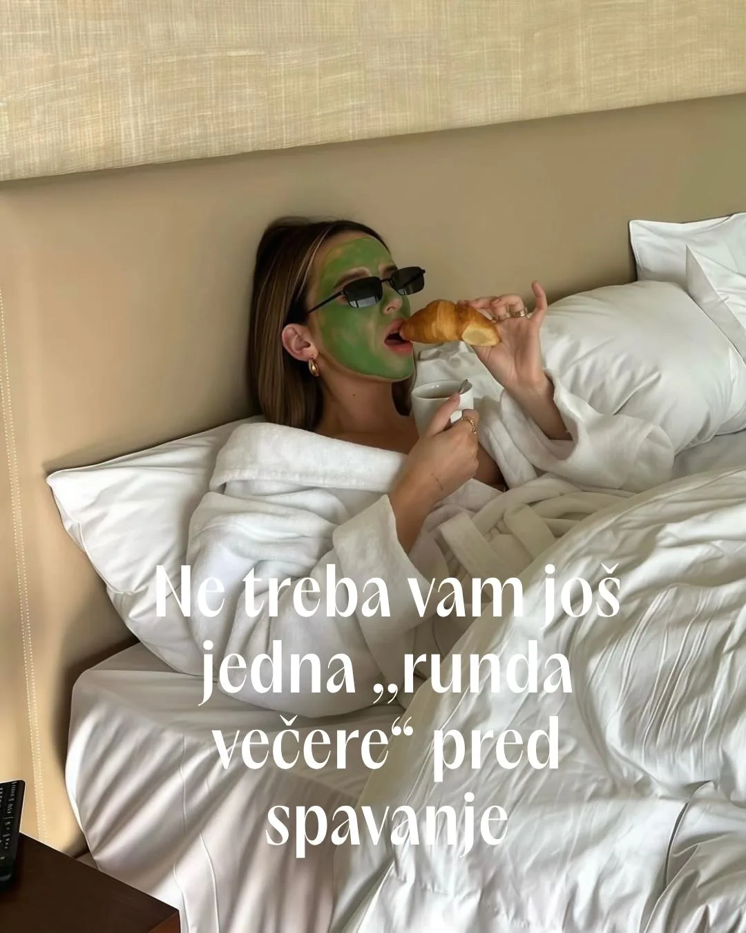 Devojka sa zelenom maskom na licu i naočarima za sunce jede kroasan u krevetu.