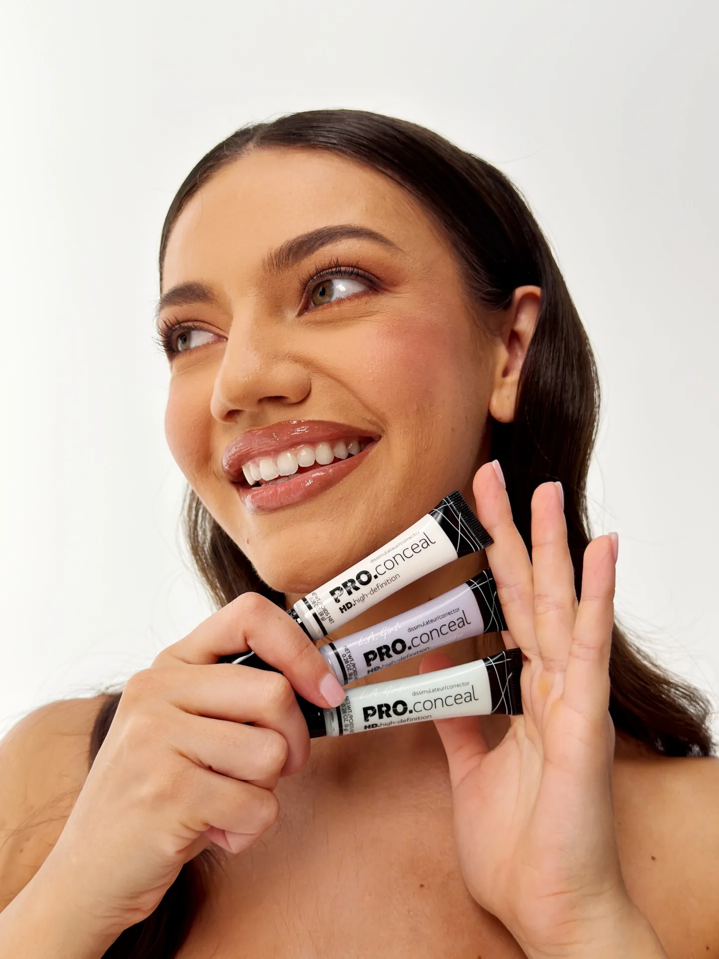 Nasmejana žena drži tri tube LA Girl PRO.conceal korektora