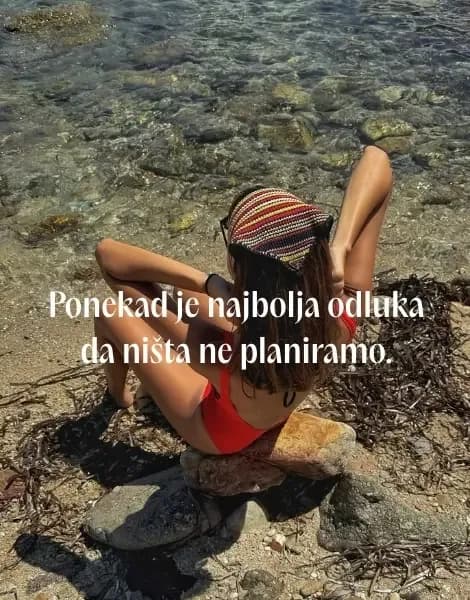 Devojka sa šarenom maramom na glavi sedi na steni pored prozirnog mora