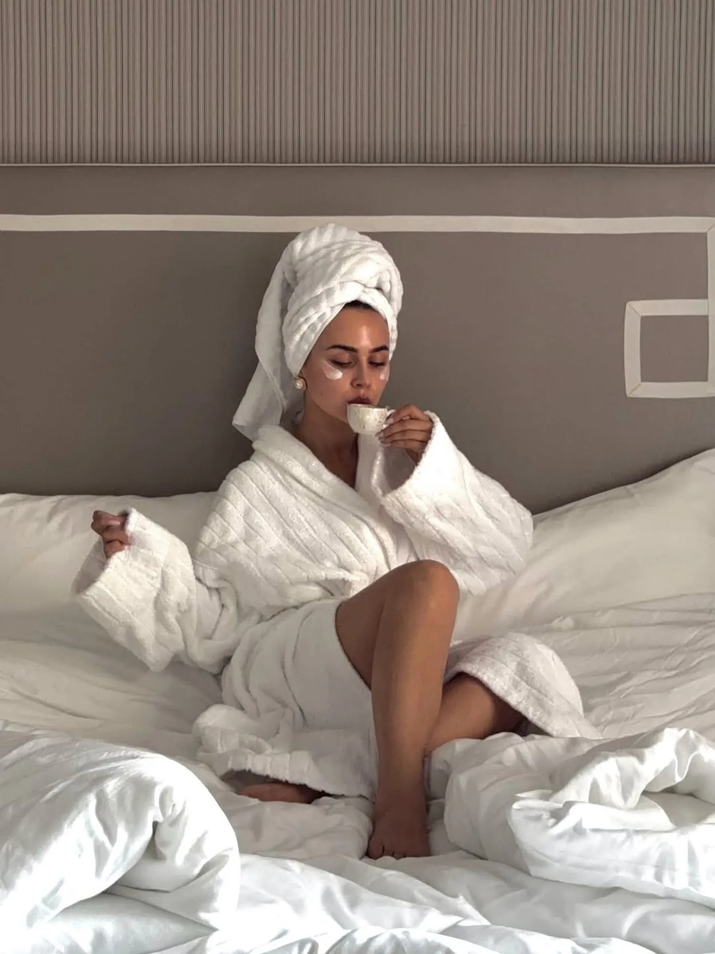 devojka u bademantilu, sa turbanom na glavi, na krevetu uživa u šoljici kafe